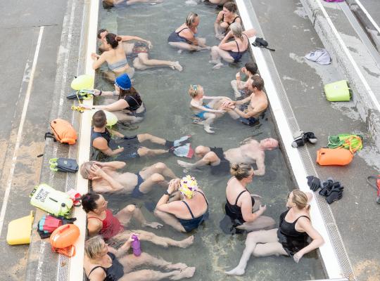 People in the hot tub at the geothermal beach in Nauthólsvík. Photo taken from above. Open-water swimming gear on the shore.