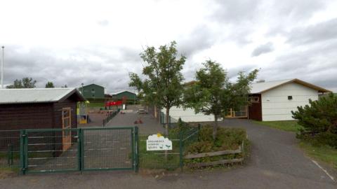 Bakkakot Preschool. Green gate in the foreground with trees on the right. 